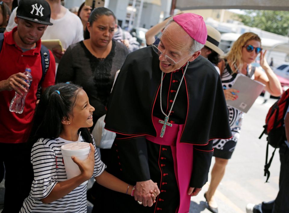 Bishop Mark J. Seitz of El Paso, Texas, shares a smile with a Honduran girl named Cesia as he walks and prays with a group of migrants at the Lerdo International Bridge in El Paso June 27, 2019. (CNS photo/Jose Luis Gonzalez, Reuters)