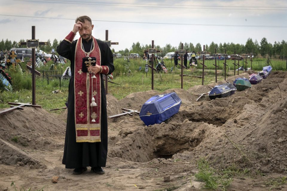 A priest prays Aug. 11 for unidentified civilians killed by Russian troops during Russian occupation in Bucha, on the outskirts of Kyiv, Ukraine. (AP/Efrem Lukatsky)